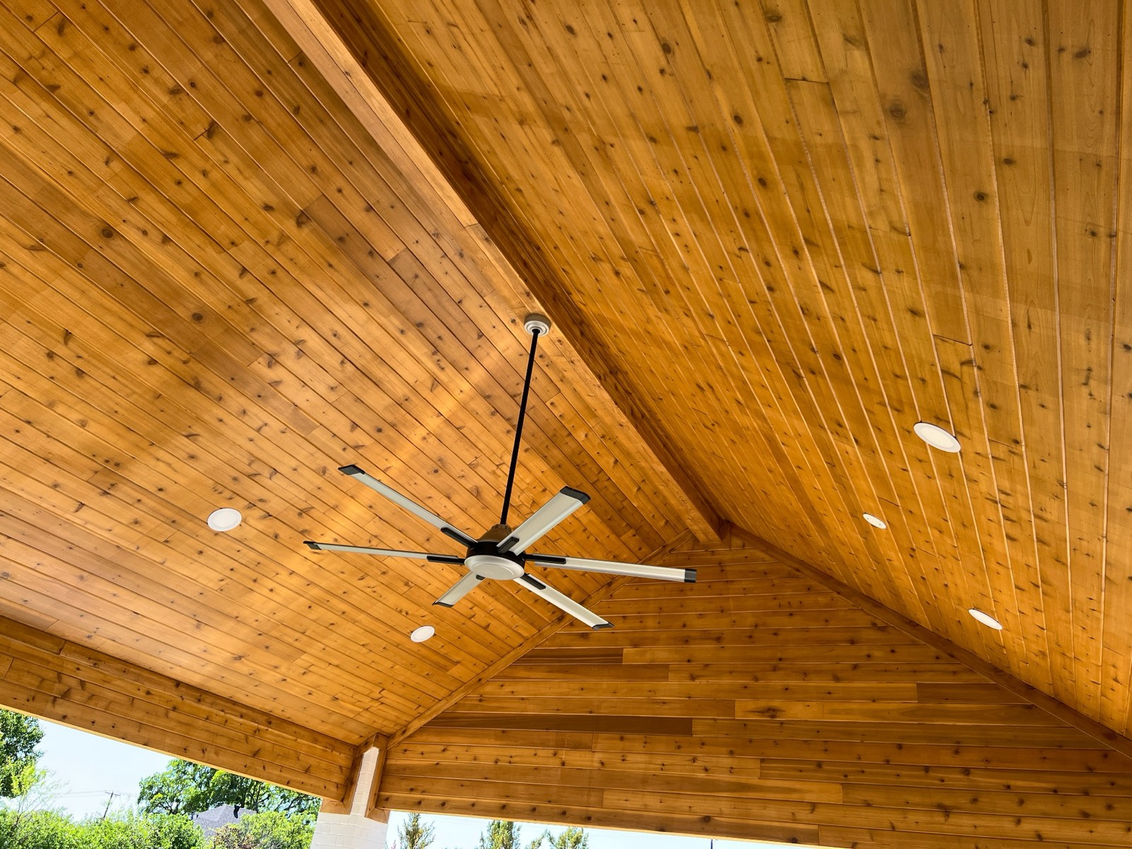 Vaulted cedar-plank patio ceiling with a large industrial fan and recessed lighting