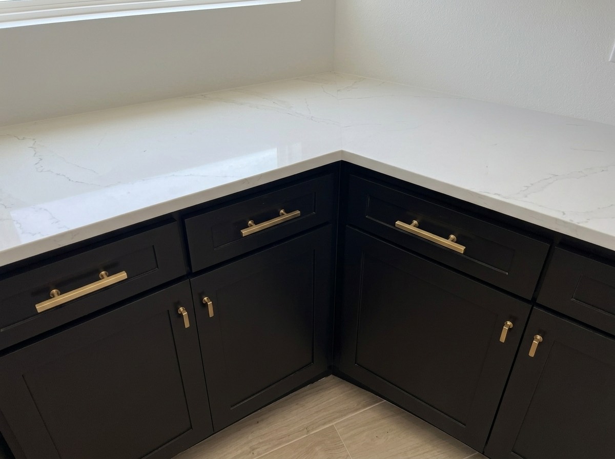 Detail of black shaker cabinetry with brushed brass hardware and a white marble countertop